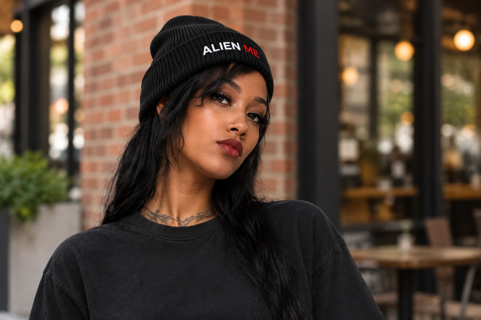 An adult female model wearing the black ALIEN ME cuff beanie outdoors with a plain unbranded top