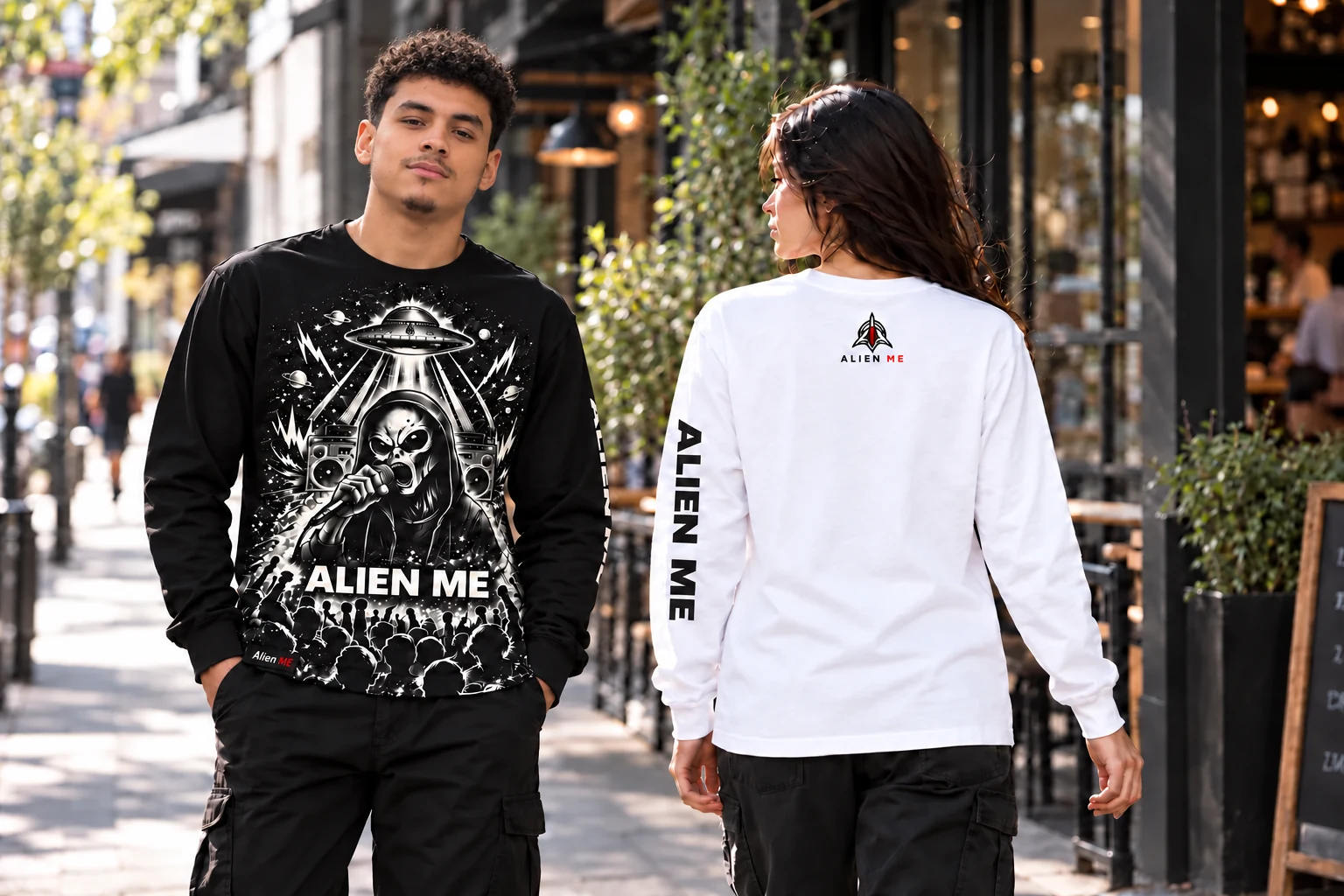 Male model wearing the black ALIEN ME Performer Long Sleeve alongside a female model showing the white version’s back logo and sleeve lettering on a city sidewalk.