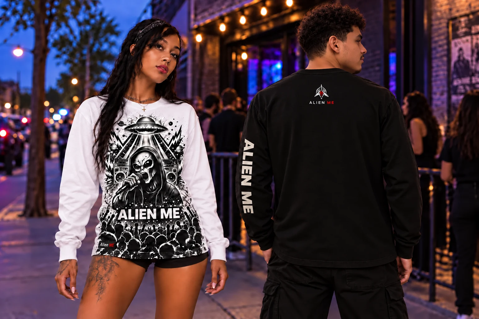Female model wearing the white Performer Long Sleeve and male model showing the black version’s back logo and ALIEN ME sleeve lettering outside a venue at dusk.
