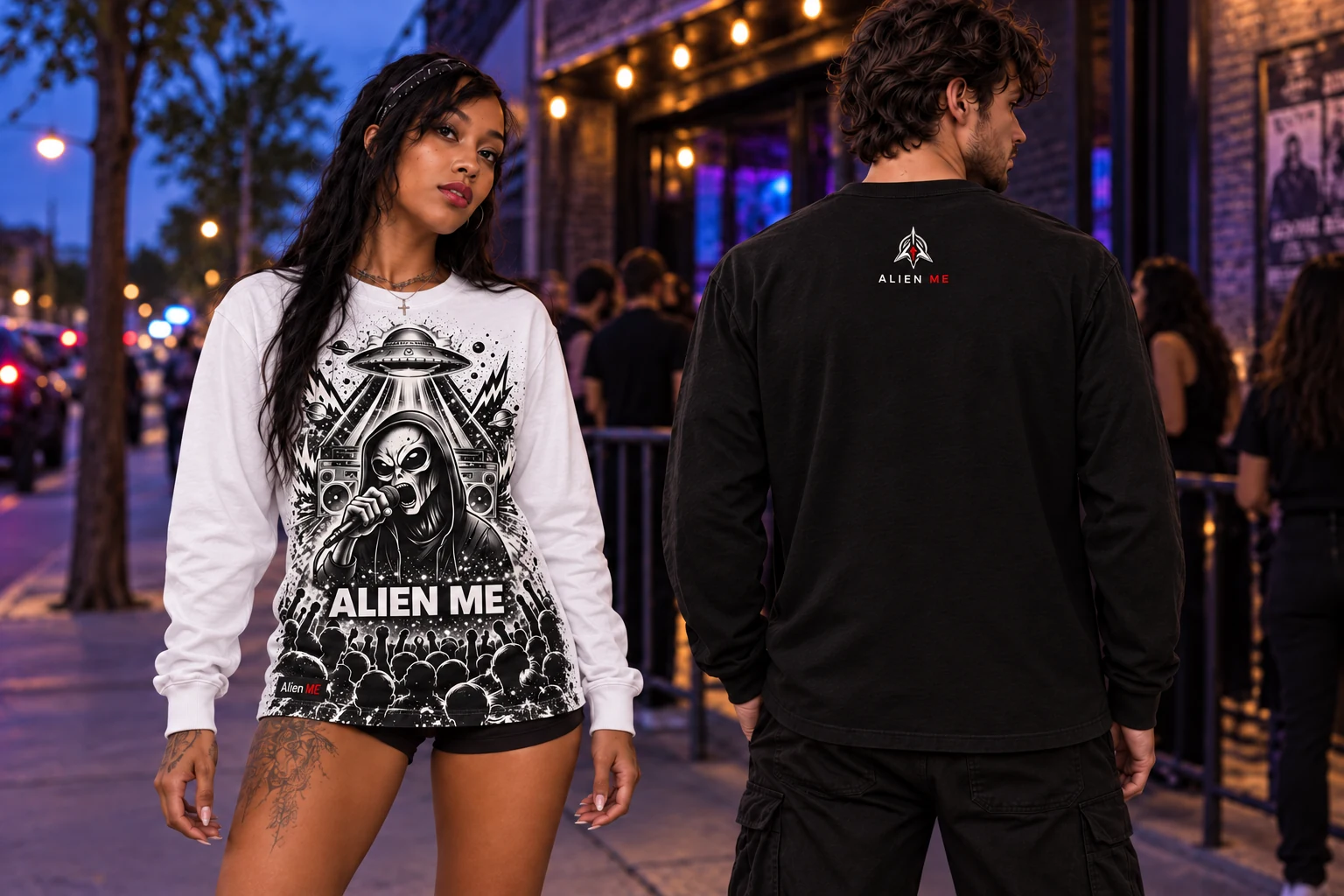 Two adult models wearing true white and black Performer Long Sleeves outside a venue at dusk, showing the full-height front illustration down to the hem, plain sleeves and a small upper-back AM mark